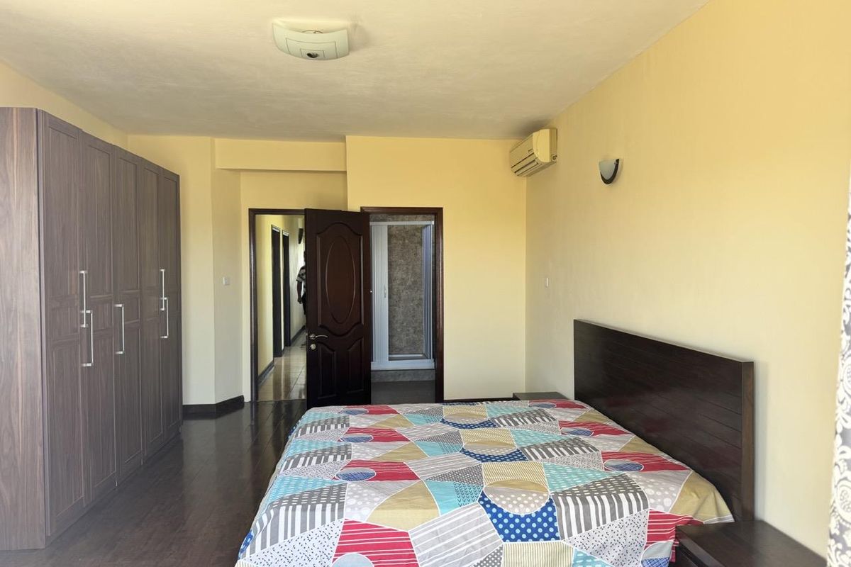 Spacious bedroom featuring dark wood laminate flooring, built-in wardrobe cabinetry, and a wall-mounted air conditioning unit.