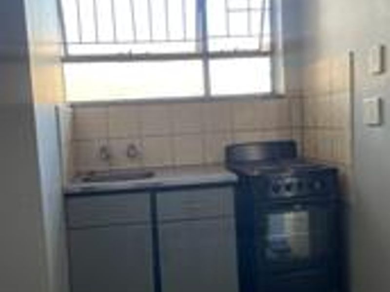 A compact kitchen area featuring basic cabinetry, a stainless steel sink, tiled splashback, and a freestanding stove with security bars on the window.