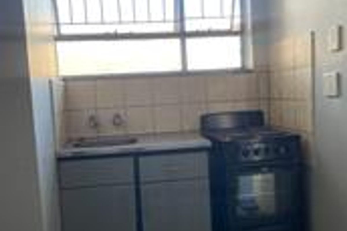 A compact kitchen area featuring basic cabinetry, a stainless steel sink, tiled splashback, and a freestanding stove with security bars on the window.