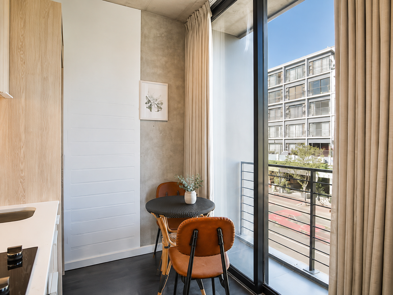 Modern open-plan apartment space featuring sleek cabinetry, integrated kitchen fixtures, and large sliding glass doors opening to a private balcony with urban views.