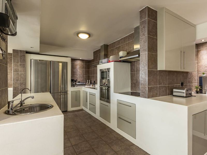 A functional kitchen featuring built-in appliances, stone countertops, tiled splashbacks, and ample cabinetry, offering a clean and practical workspace.