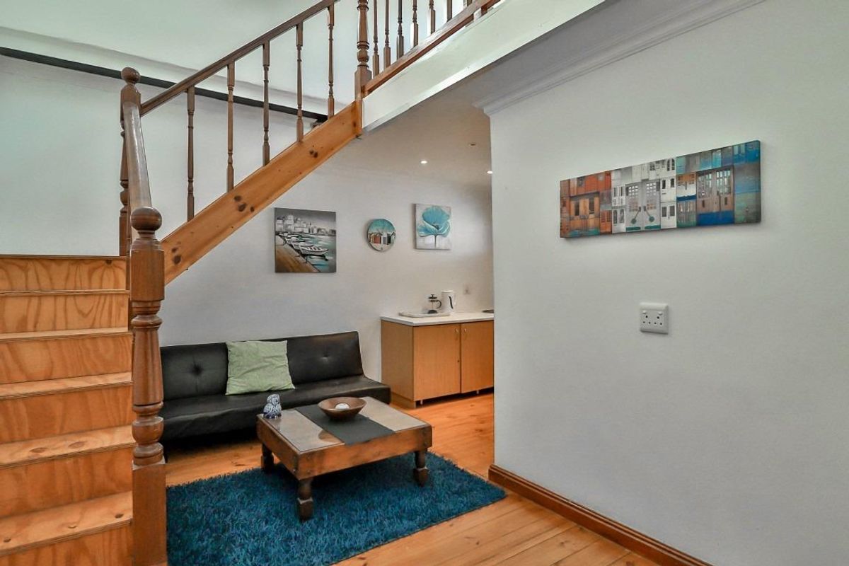 A living area featuring timber flooring and a wooden staircase with balustrade, leading to an adjacent kitchenette area.