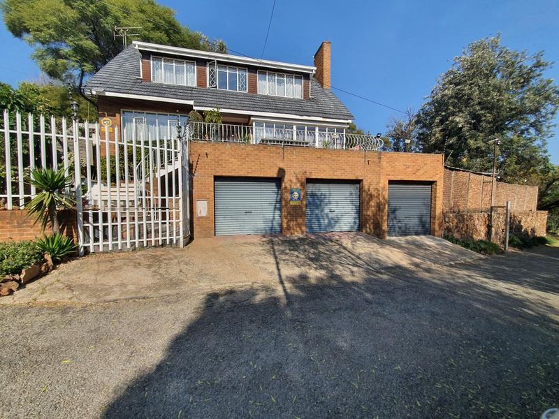 Front elevation of a multi-level brick house featuring a triple garage, balcony, and secure perimeter fencing.
