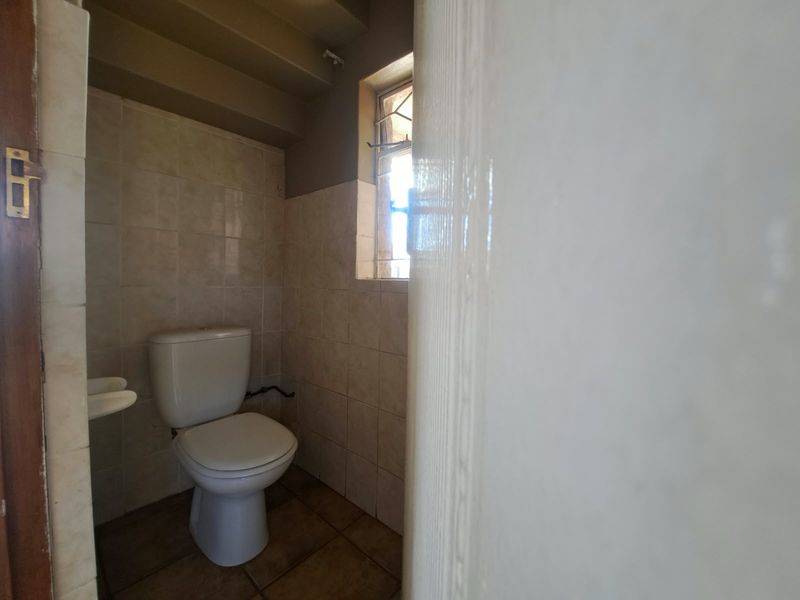 A compact, dated bathroom featuring ceramic wall and floor tiles, a standard toilet, and a small basin.