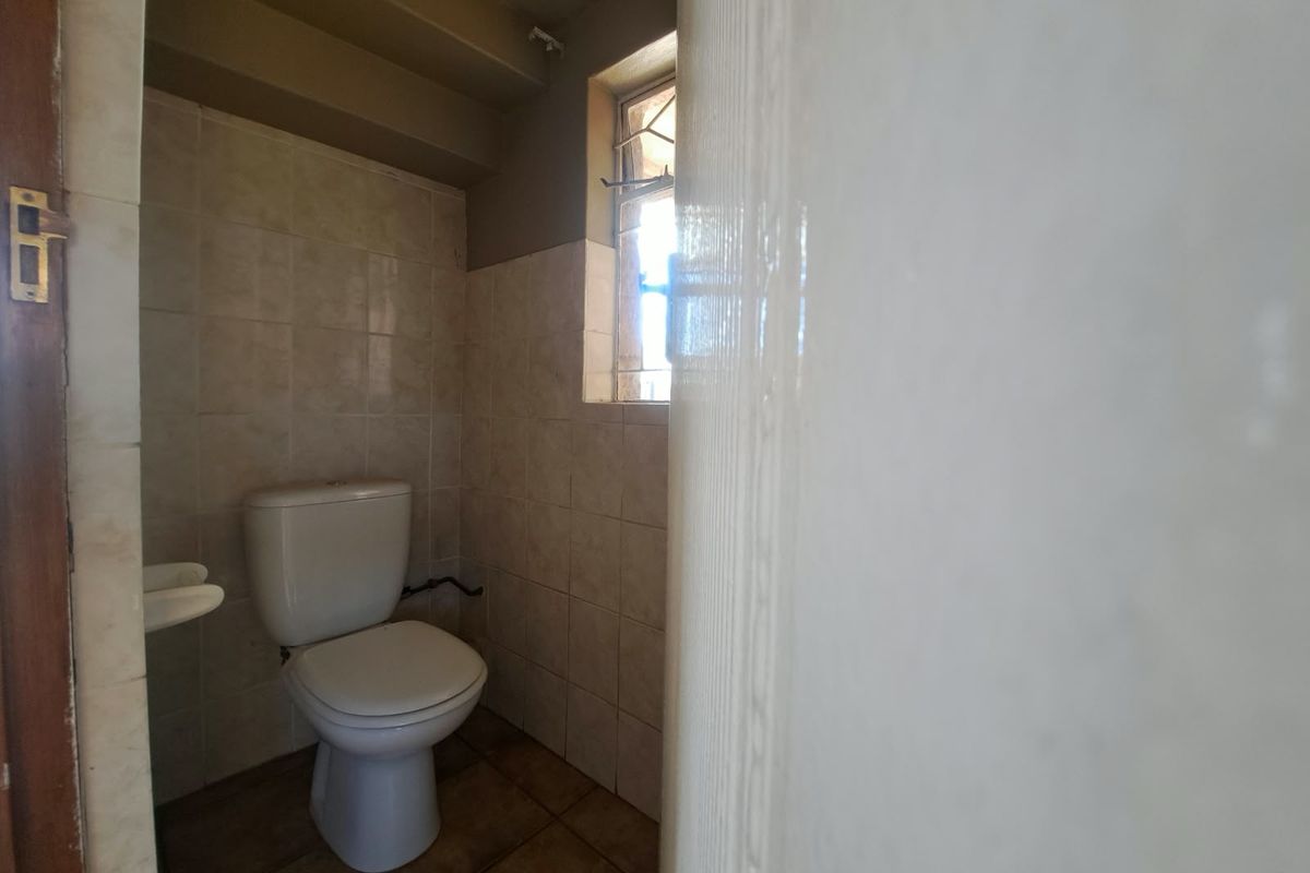 A compact, dated bathroom featuring ceramic wall and floor tiles, a standard toilet, and a small basin.