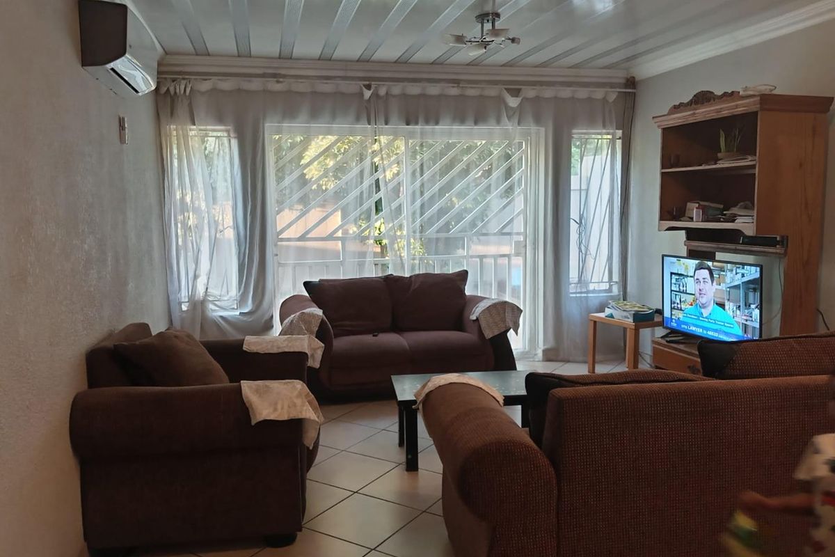 A comfortable living room featuring tiled flooring, a wall-mounted air conditioning unit, and large sliding glass doors with security bars leading to the exterior.
