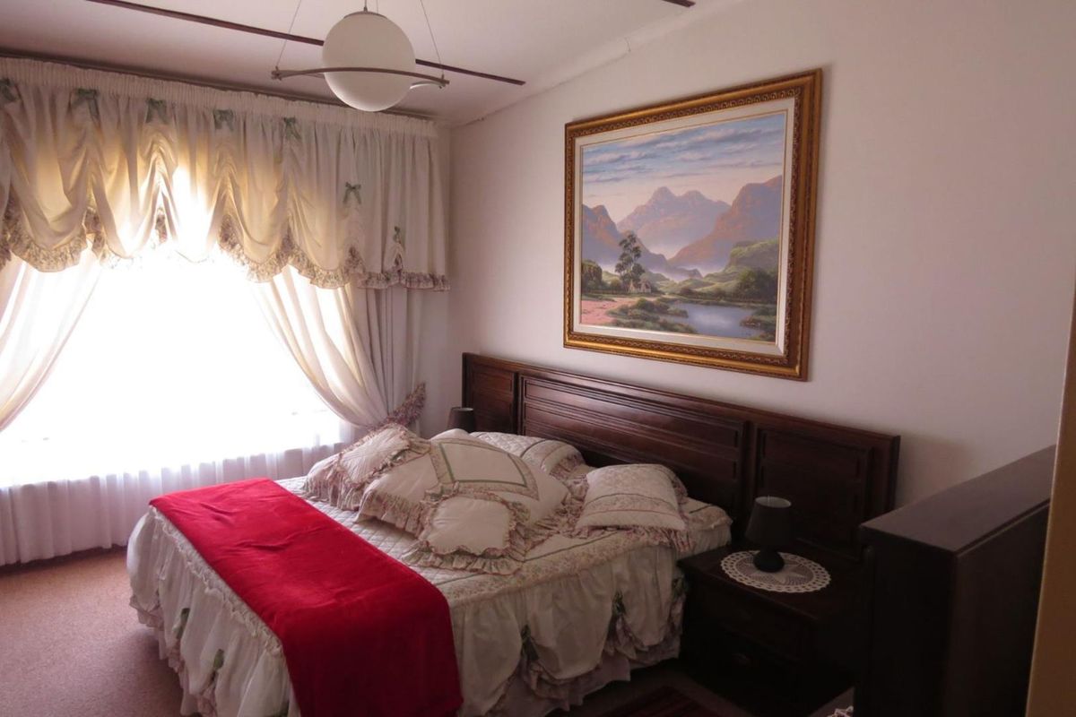 A bedroom featuring a built-in wooden headboard and a large window with draped curtains.
