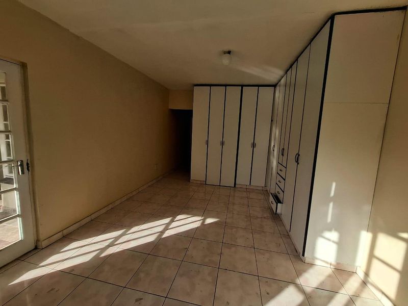 An empty bedroom featuring tiled flooring, built-in cupboards, and a glass panel door leading to the exterior.