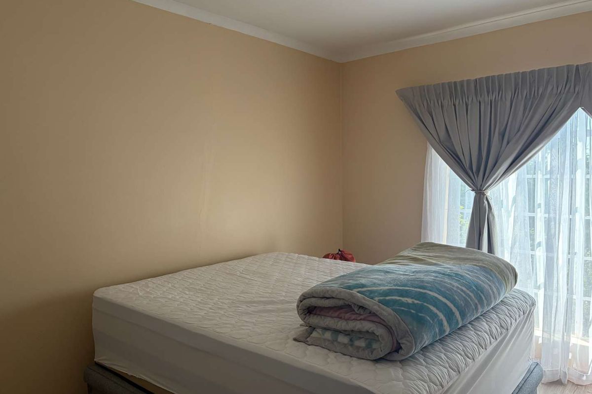 A bedroom featuring neutral wall tones, a window with curtain treatments, and laminate flooring.