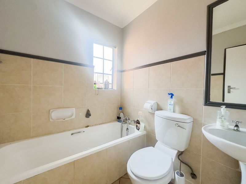 A functional bathroom featuring a bathtub, pedestal basin, and toilet with neutral wall tiling and a window for natural light.