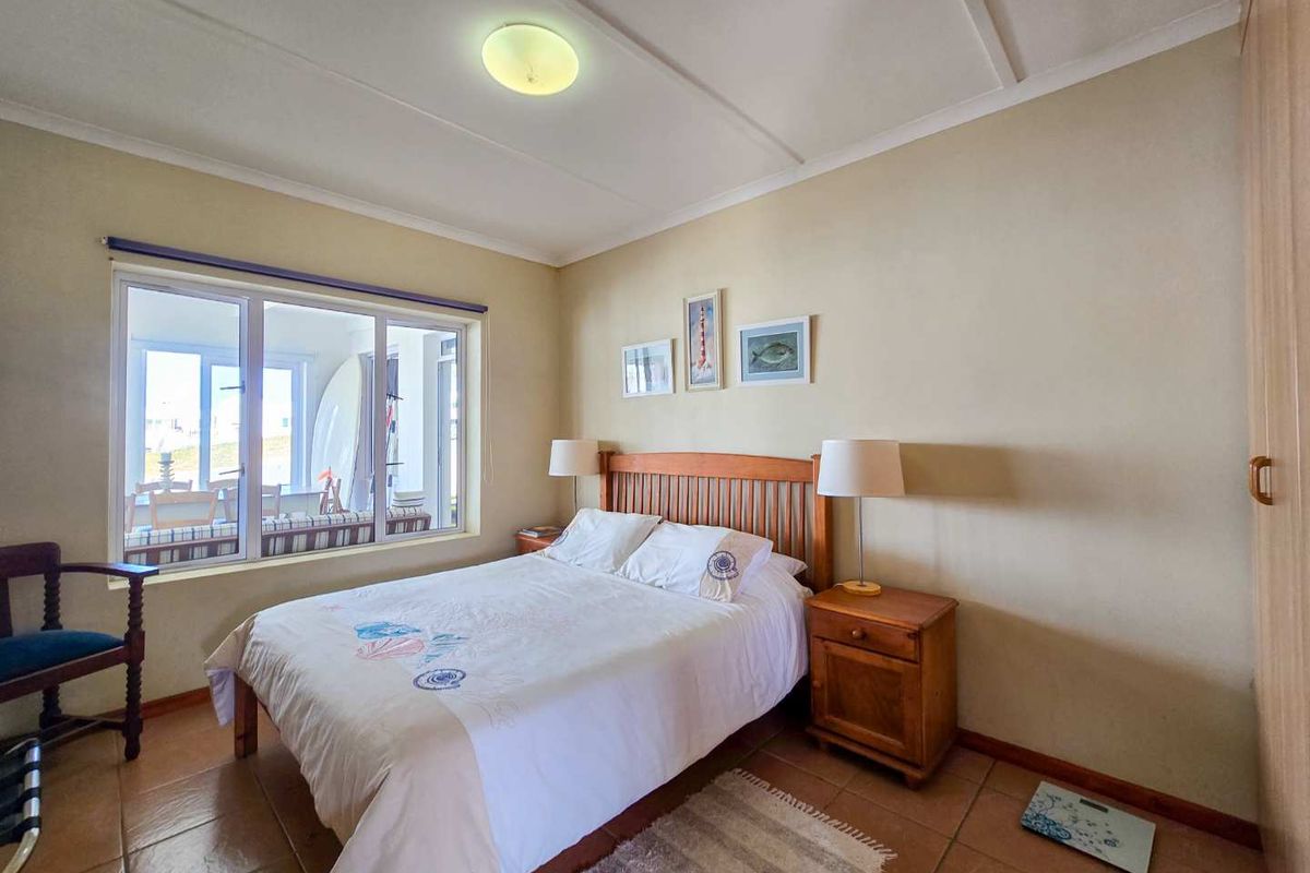A functional bedroom featuring tiled flooring, a built-in wardrobe, and a large window allowing natural light into the space.