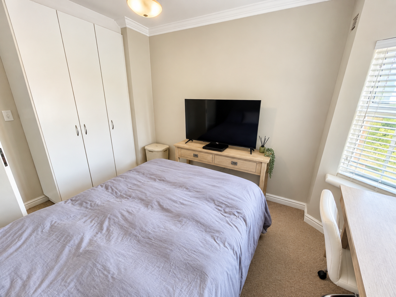 A well-maintained bedroom featuring neutral walls, carpet flooring, built-in wardrobes, and venetian blinds, offering a clean and functional living space.