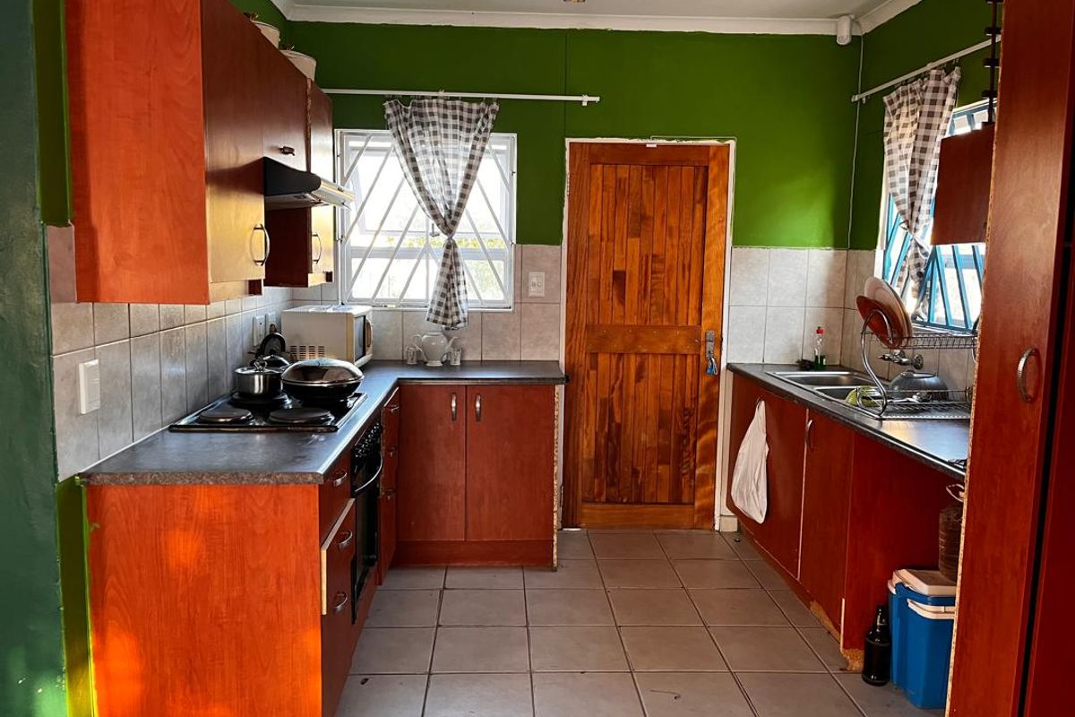 A functional kitchen featuring wood-look cabinetry, tiled splashbacks, a built-in hob and oven, and tiled flooring with direct access to the exterior.