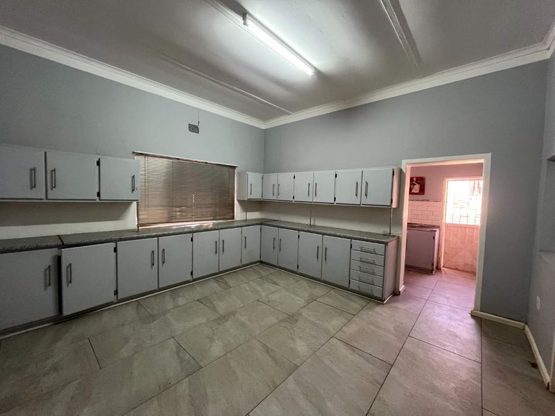 A spacious, empty kitchen featuring extensive built-in cabinetry, tiled flooring, and a functional layout with an adjacent scullery area.