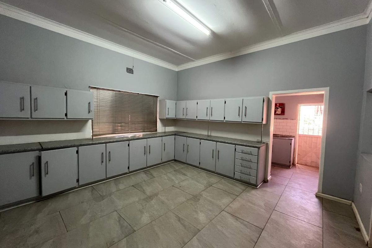 A spacious, empty kitchen featuring extensive built-in cabinetry, tiled flooring, and a functional layout with an adjacent scullery area.