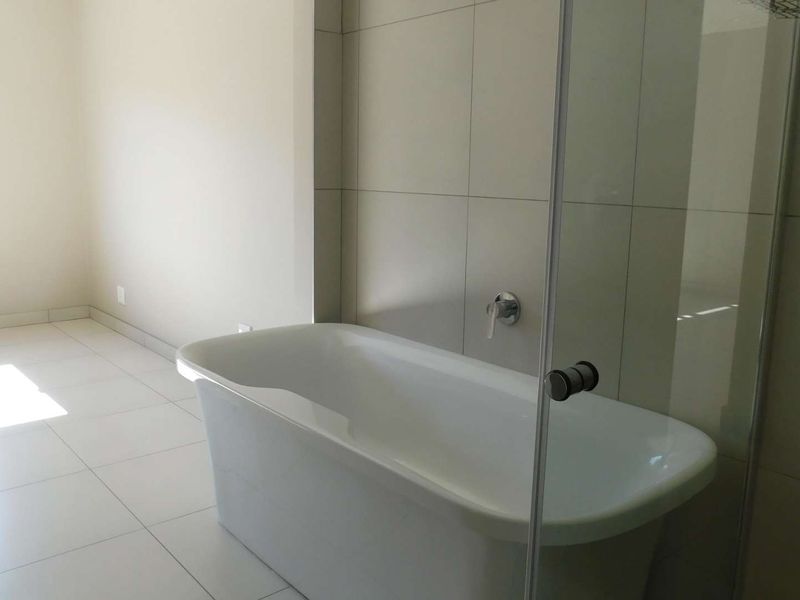 A bright, modern bathroom featuring a freestanding bathtub, a glass-enclosed shower area, and neutral floor-to-ceiling wall tiles.