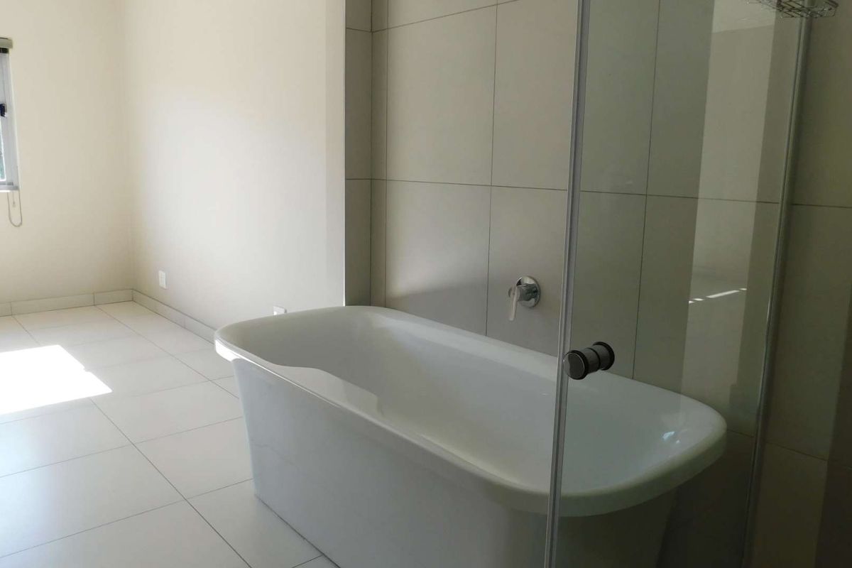 A bright, modern bathroom featuring a freestanding bathtub, a glass-enclosed shower area, and neutral floor-to-ceiling wall tiles.