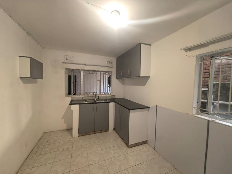 A compact, empty kitchen featuring grey built-in cabinetry, laminate countertops, a stainless steel sink, and tiled flooring, ready for renovation or personalization.
