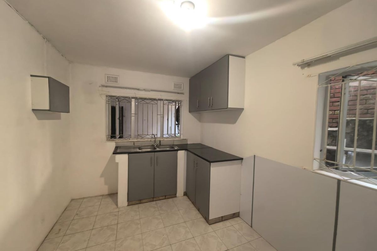A compact, empty kitchen featuring grey built-in cabinetry, laminate countertops, a stainless steel sink, and tiled flooring, ready for renovation or personalization.