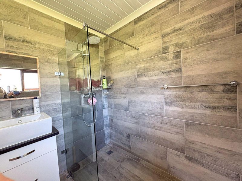 Modern bathroom featuring a glass-enclosed walk-in shower with rain shower head, contemporary vessel sink vanity, and neutral wood-look wall tiling.