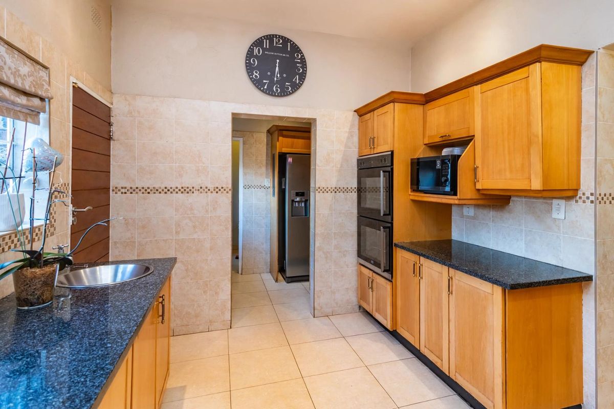A functional kitchen featuring wooden cabinetry, granite countertops, a double wall oven, and a built-in microwave, with tiled finishes throughout.
