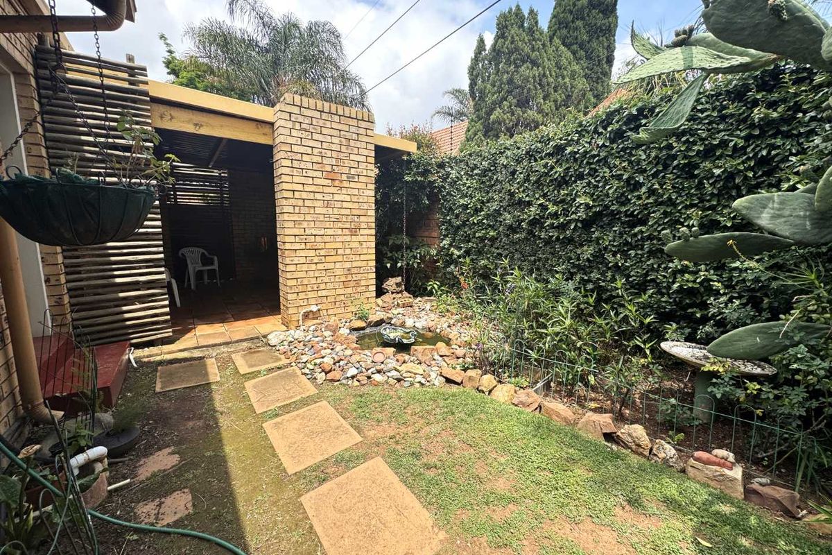A private rear garden featuring a covered patio, brick pillar, small decorative pond, and established perimeter hedging.