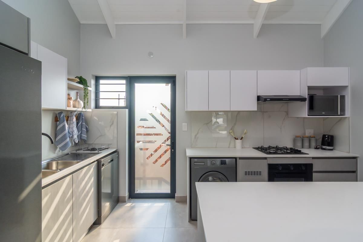 Modern kitchen featuring white cabinetry, marble-look splashbacks, integrated appliances, gas hob, and a vaulted ceiling with exposed rafters.
