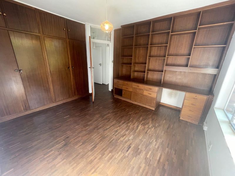Bedroom featuring extensive built-in wooden cabinetry, shelving, and a desk, complemented by parquet flooring. Requires minor repairs to wall finishes.