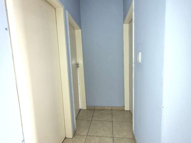 A simple, functional hallway featuring neutral tiled flooring and multiple internal access doors.