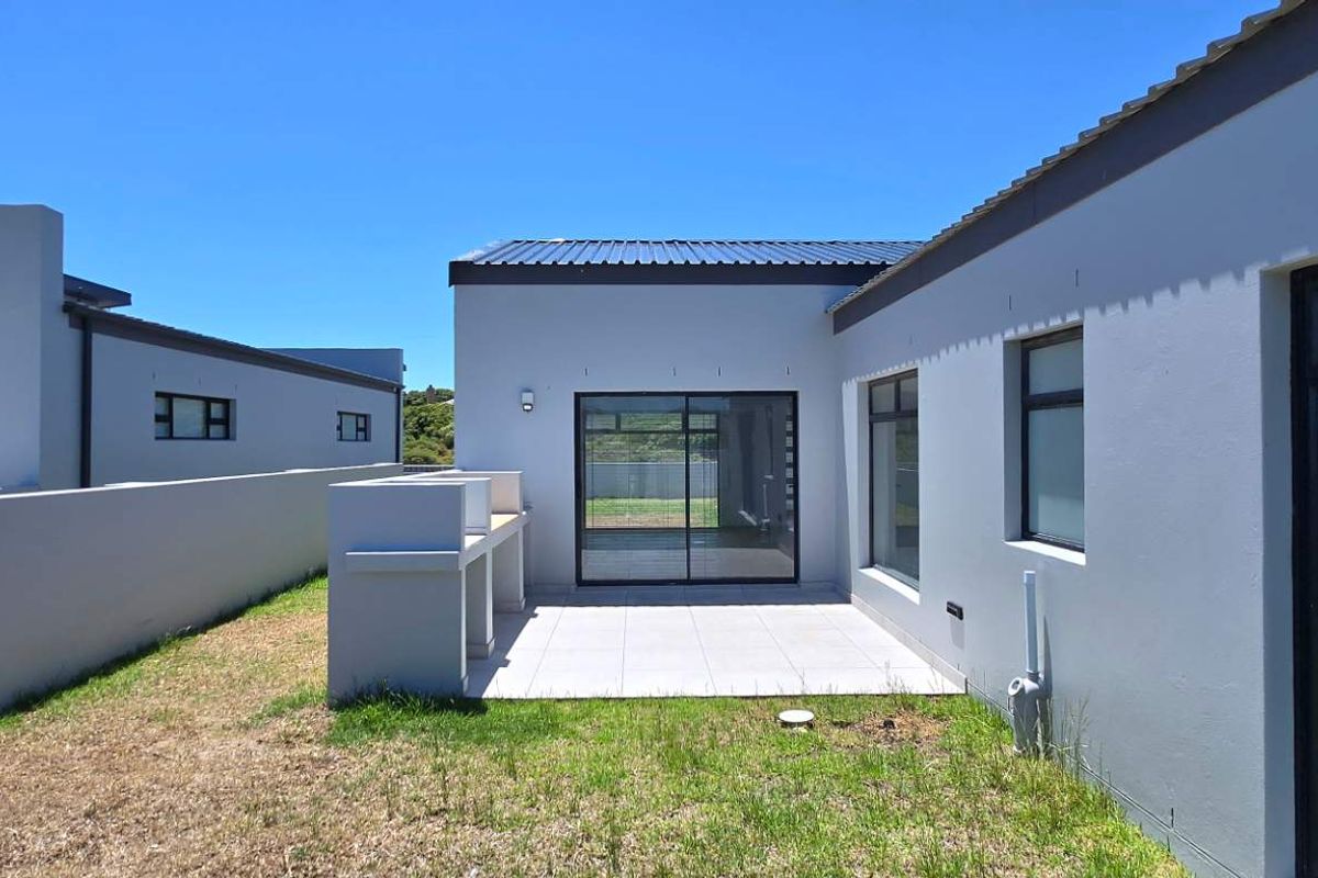 Rear exterior view featuring a paved patio area with a built-in braai, accessible via sliding glass doors from the main living space.