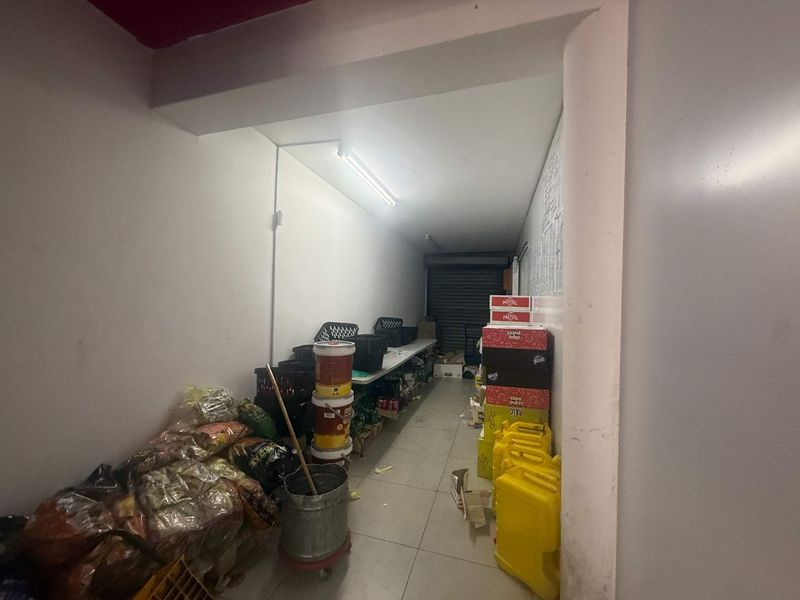 A functional utility or storage space featuring tiled flooring, fluorescent lighting, and a secure roller shutter door access point.