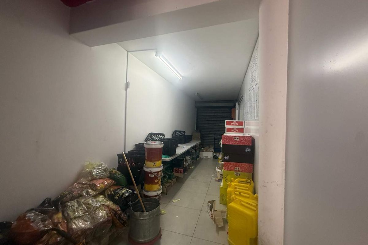 A functional utility or storage space featuring tiled flooring, fluorescent lighting, and a secure roller shutter door access point.