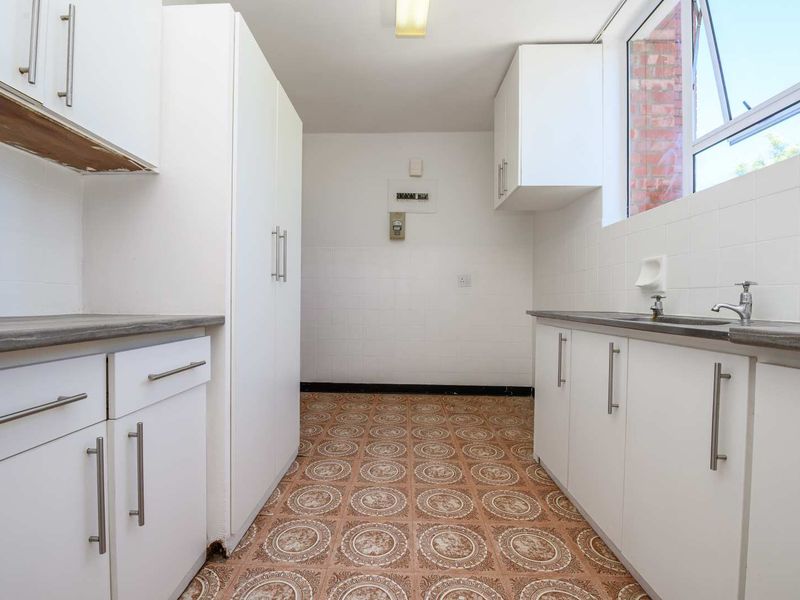 A functional, empty kitchen featuring white cabinetry, laminate countertops, a stainless steel sink, and patterned vinyl flooring.