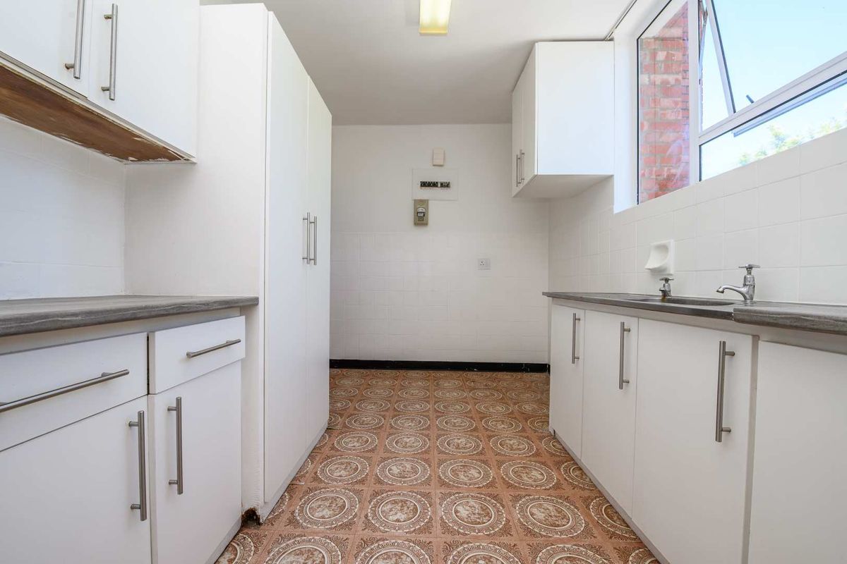 A functional, empty kitchen featuring white cabinetry, laminate countertops, a stainless steel sink, and patterned vinyl flooring.