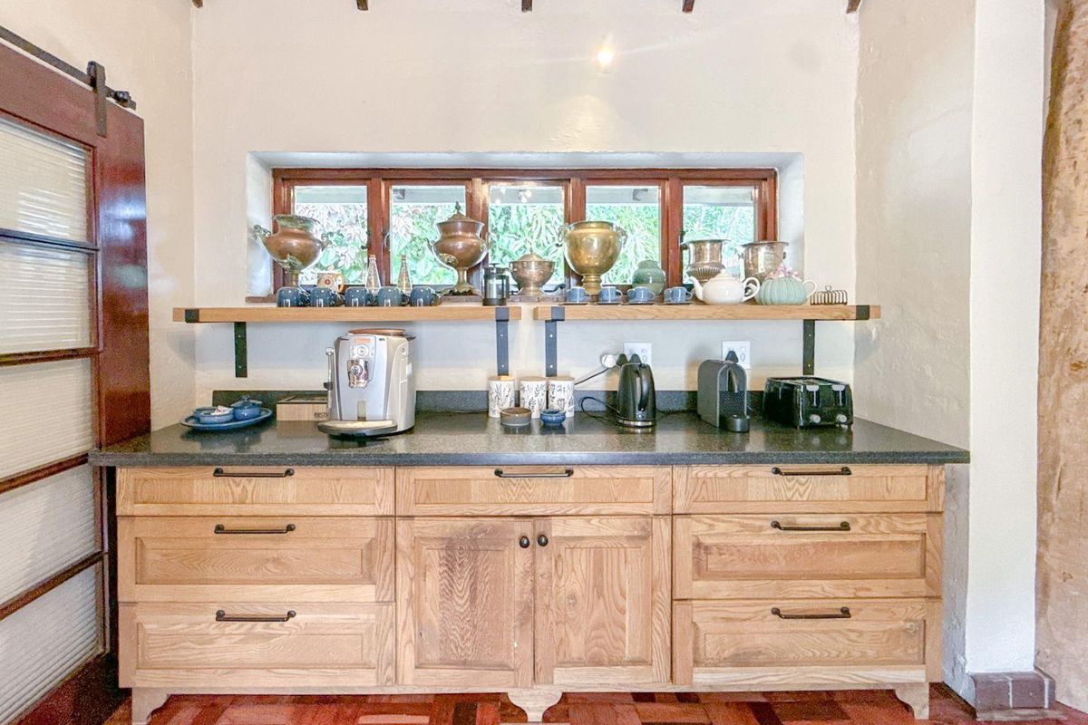 A well-appointed kitchen area featuring custom light oak cabinetry, dark stone countertops, open shelving, and exposed timber ceiling beams.