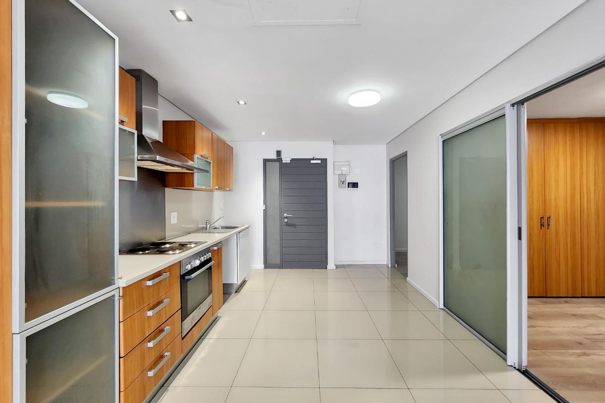 Modern kitchen featuring wood-finish cabinetry, stainless steel appliances, tiled flooring, and sleek frosted glass sliding doors leading to an adjacent room.