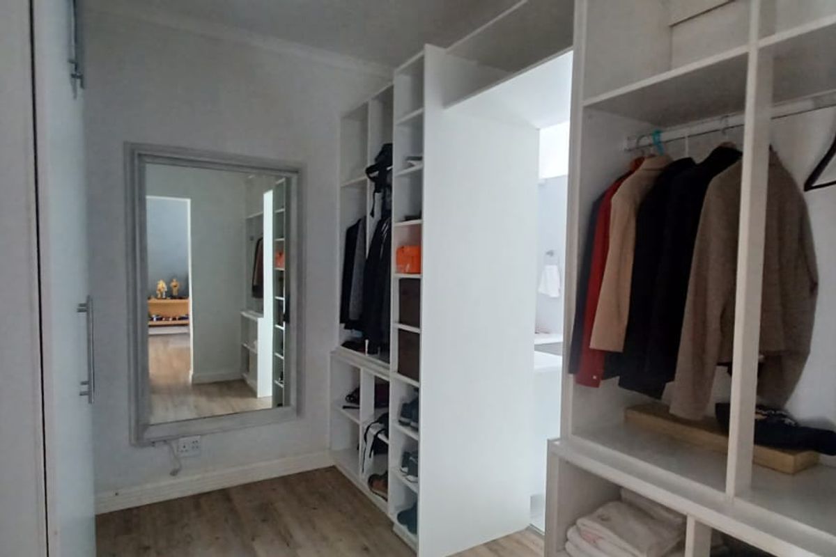 A well-organized walk-in closet featuring extensive built-in white cabinetry, laminate flooring, and a wall-mounted mirror.