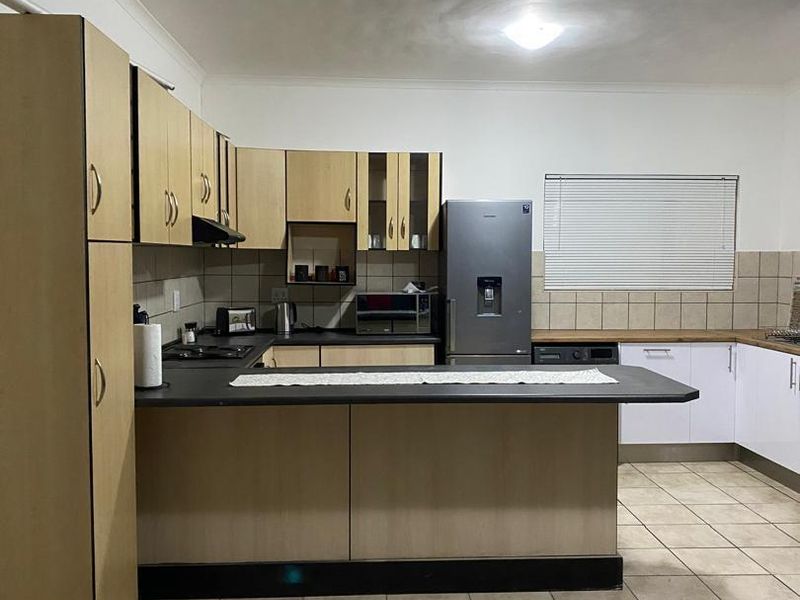 Functional kitchen featuring laminate cabinetry, dark countertops, ceramic tile flooring, and a breakfast bar layout with integrated hob and extractor fan.