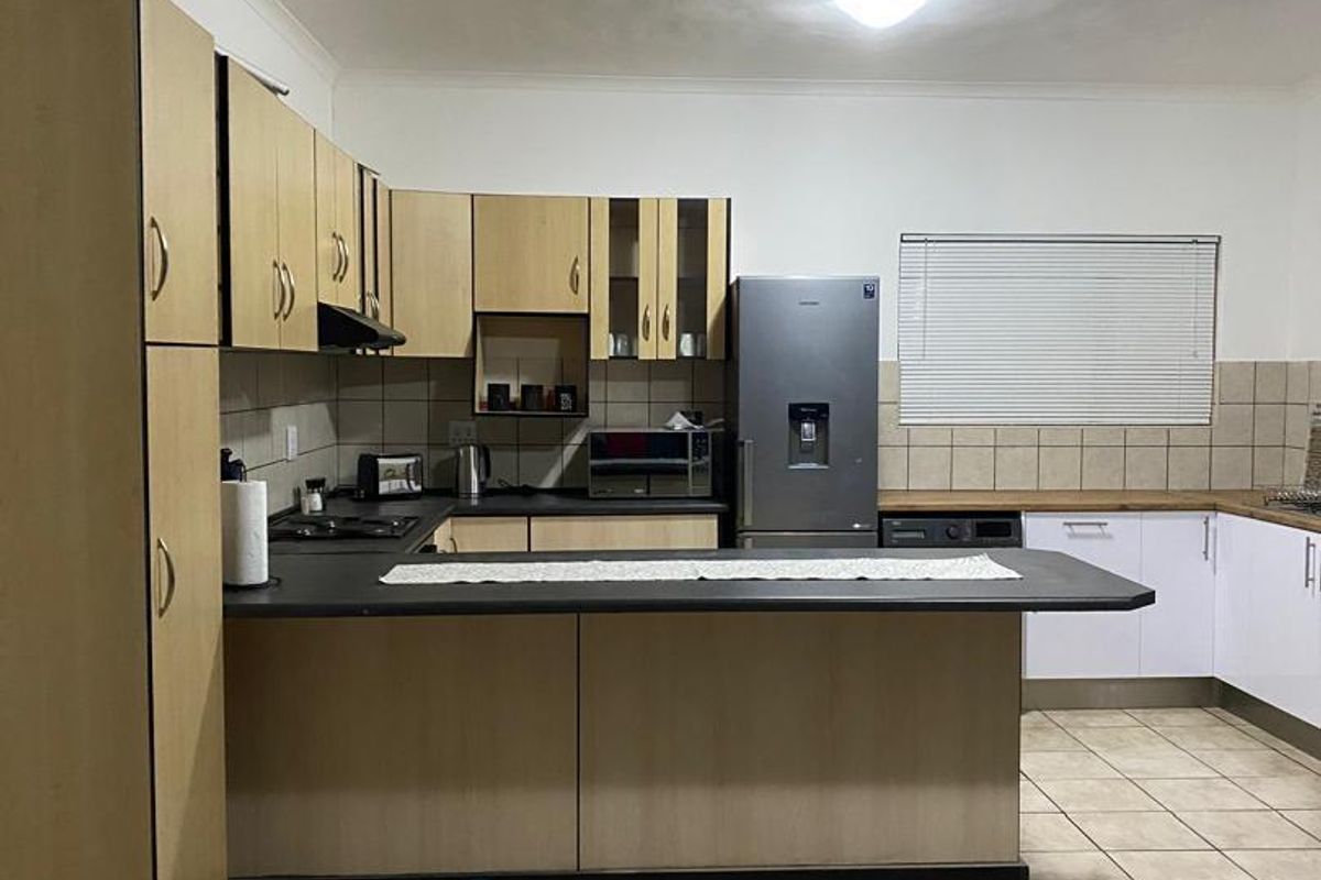 Functional kitchen featuring laminate cabinetry, dark countertops, ceramic tile flooring, and a breakfast bar layout with integrated hob and extractor fan.