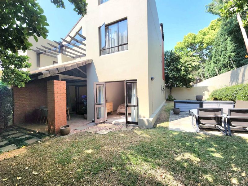 Rear view of the apartment featuring a covered patio, brick detailing, and a private garden area with paved access.
