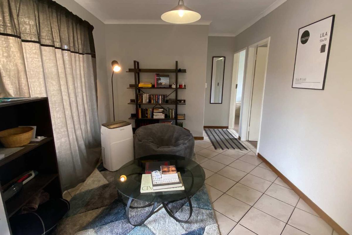 A cozy living room featuring tiled flooring, neutral wall tones, and access to adjacent rooms through a central hallway.