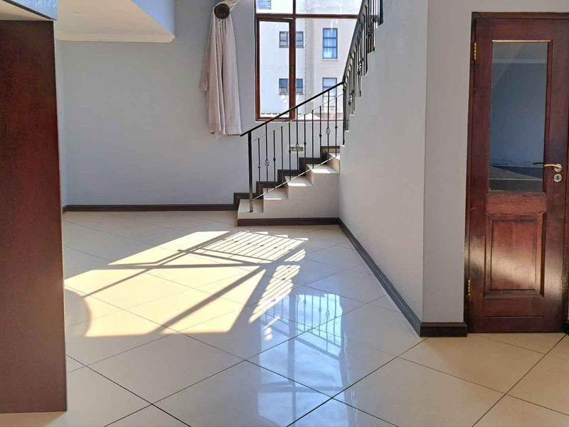 Spacious open-plan living area featuring polished tile flooring, a staircase with wrought iron balustrade, and a classic timber door.