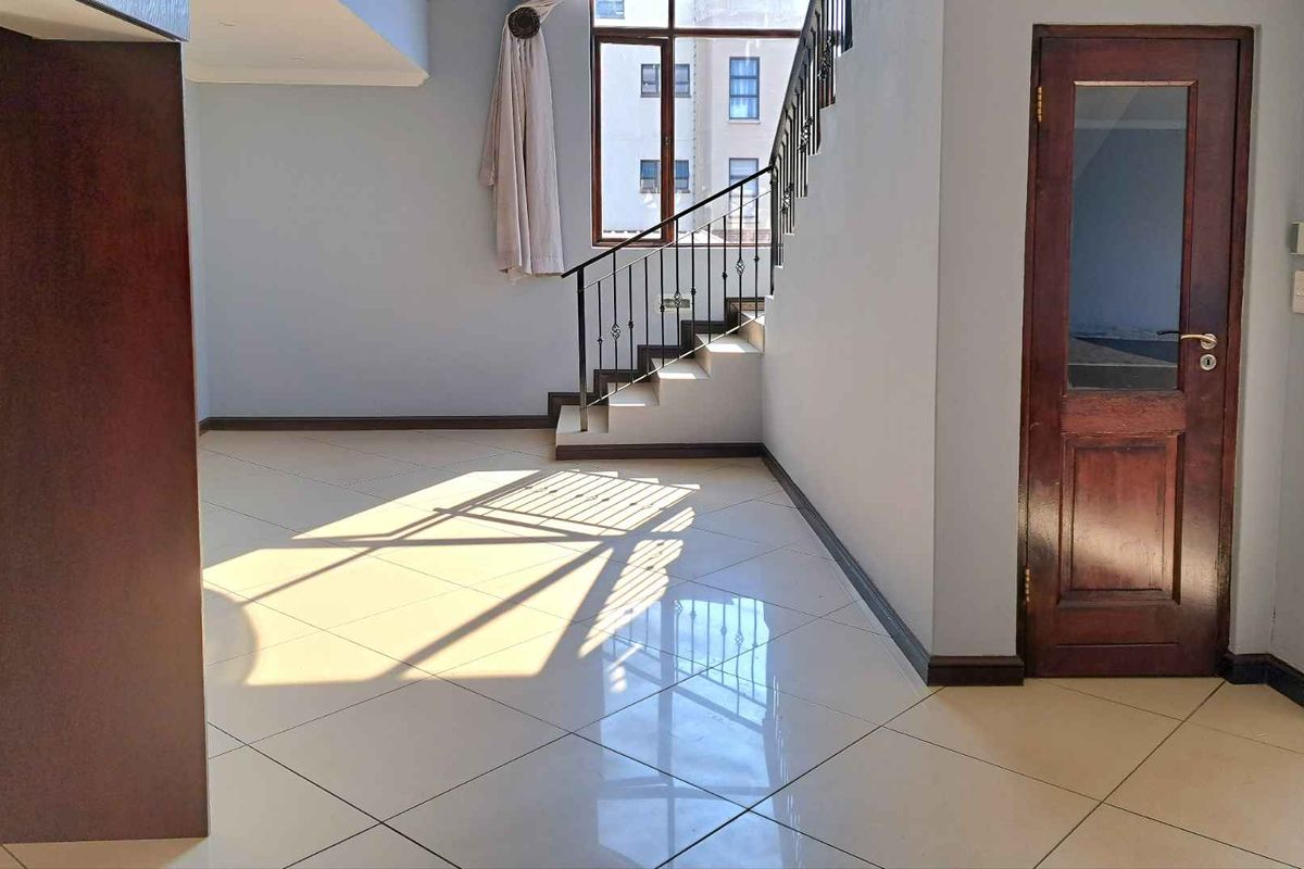 Spacious open-plan living area featuring polished tile flooring, a staircase with wrought iron balustrade, and a classic timber door.
