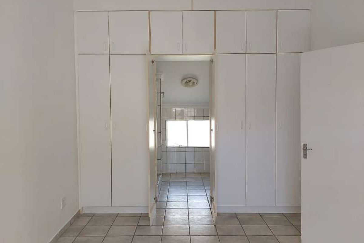 A bedroom featuring built-in floor-to-ceiling cupboards and tiled flooring, with an open doorway leading to an adjoining bathroom.