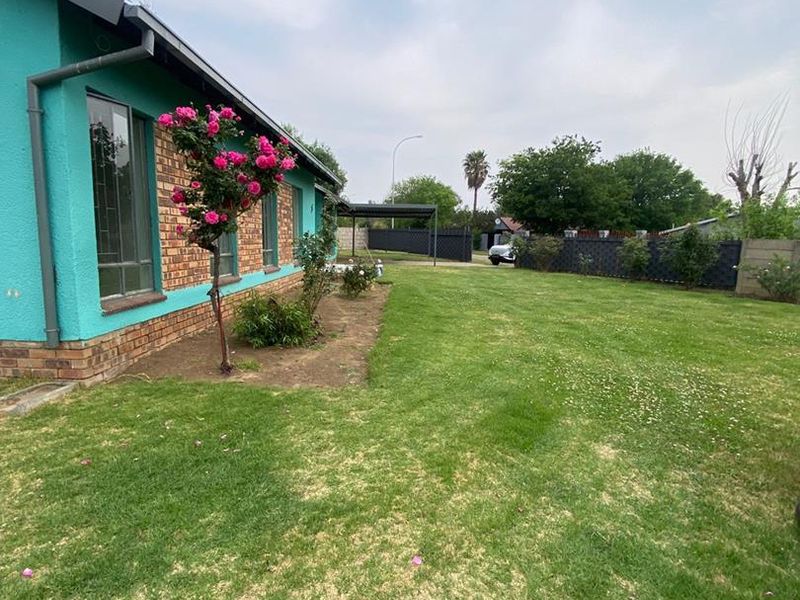 A view of the rear garden and side elevation of the house, featuring a lawn, brick and painted plaster exterior, and perimeter fencing.