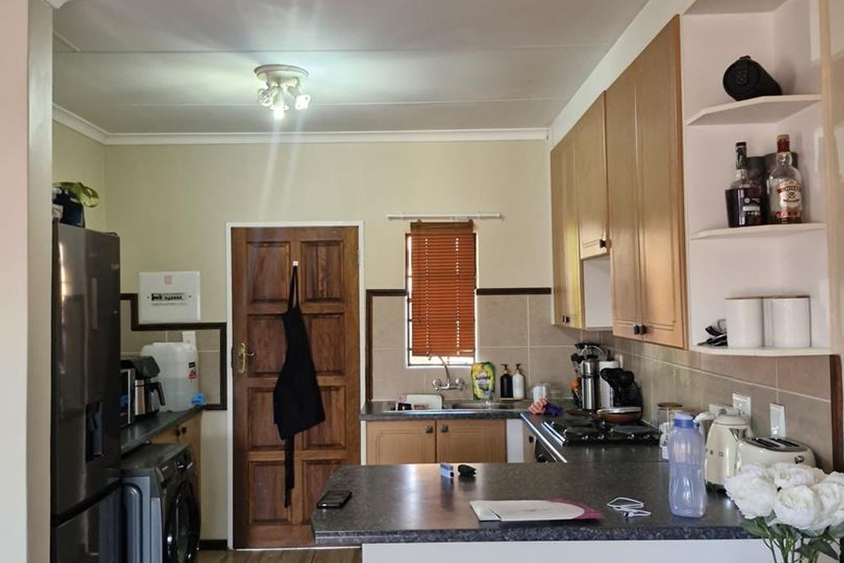 A functional kitchen featuring wood-toned cabinetry, a breakfast bar, tiled splashbacks, and integrated laundry space with direct access to a wooden door.