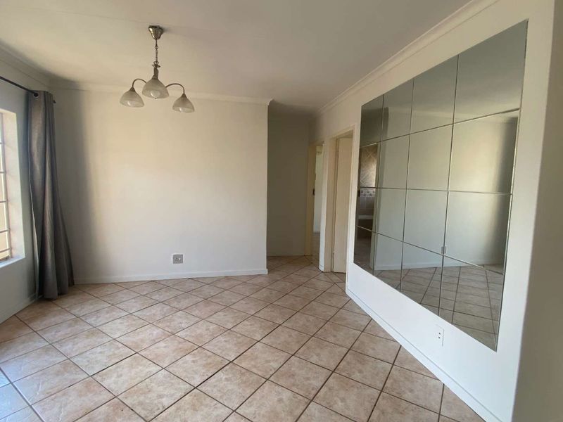 A bright, empty living area featuring neutral tiled flooring, a large decorative mirrored wall, and classic coved cornicing.