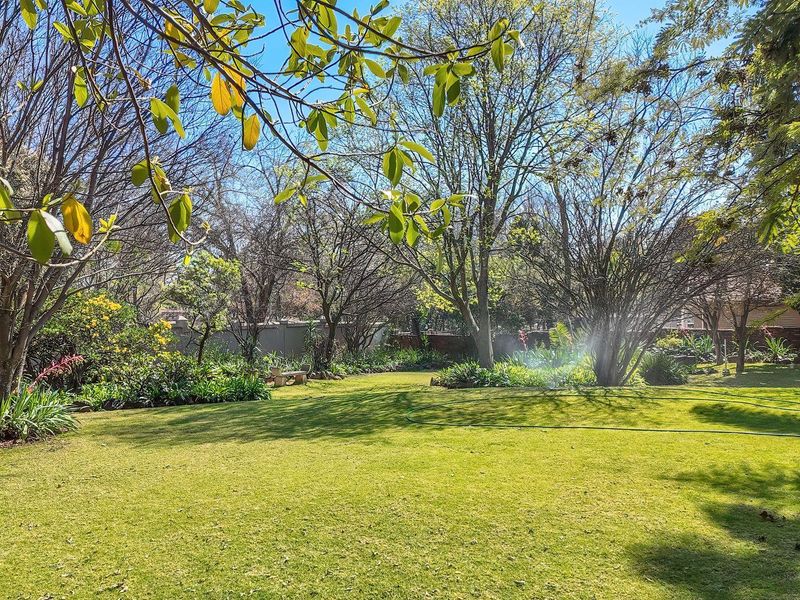 A spacious, well-maintained garden featuring a lush green lawn, mature trees, and a secure perimeter wall.