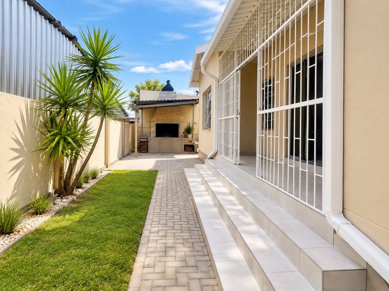 A well-maintained rear exterior featuring a paved walkway, a built-in braai area, and tiled steps leading to the home with secure metal gates.