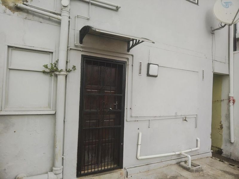 Rear exterior view showing a security door, external plumbing, and wall-mounted fixtures on a weathered facade.